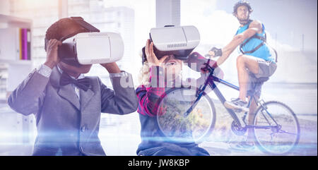 Montare l'uomo in bicicletta su terreno roccioso contro i bambini imitando la gente di affari che indossa la realtà virtuale auricolare Foto Stock