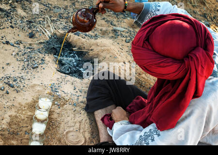Uomo marocchino con turbante rosso prepara il tradizionale tè alla menta nel deserto. Foto Stock