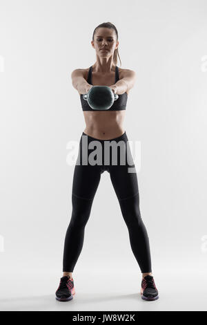 Vista frontale retroilluminato silhouette di forte montare donna kettlebell facendo oscillare l'esercizio. Dissaturato corpo pieno ritratto su sfondo grigio. Foto Stock