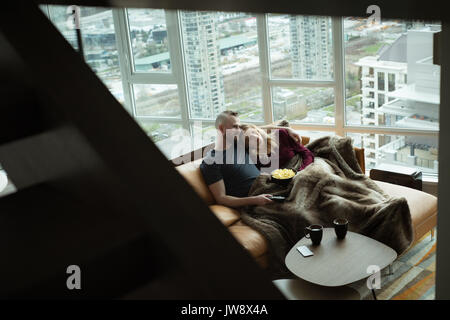 Giovane rilassante sul divano guardando la tv nel salotto di casa Foto Stock