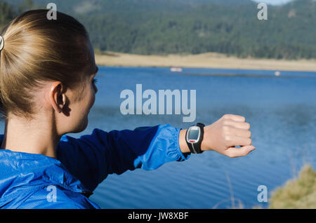 Vista laterale della donna che guarda un orologio da polso mentre in piedi contro il lago Foto Stock