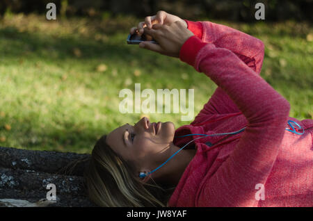 Ravvicinata di un escursionista femmina usando il telefono mentre giaceva sulla parete di ritegno nella foresta Foto Stock