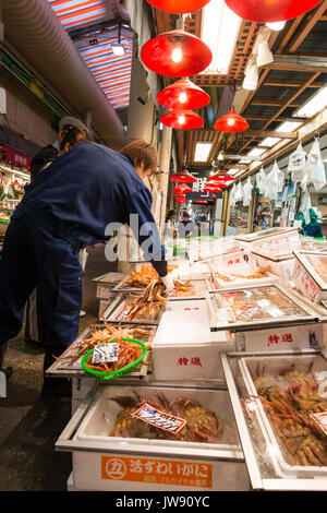 A basso angolo di visione del proprietario di stallo arrangiare grossi granchi di arancione in contenitori su una fase di stallo nel Omicho indoor mercato alimentare a Kanazawa in Giappone. Foto Stock