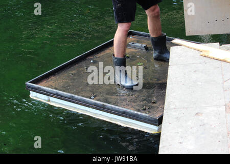 Square zattera per ponte opere di riparazione galleggia sull'acqua. Il lavoratore è su una zattera e vincola una cassaforma di legno per la ringhiera per decorare la vacanza. Foto Stock