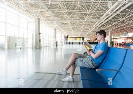 Giovane uomo in attesa nella sala partenze di un aeroporto la lettura di un libro Foto Stock