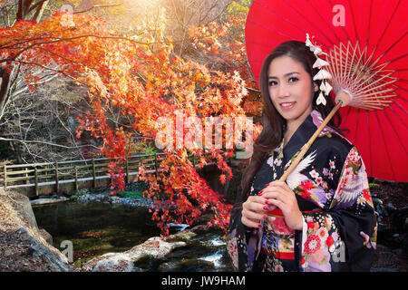 Donna asiatica indossando il tradizionale kimono giapponese con ombrello rosso in autunno. Foto Stock