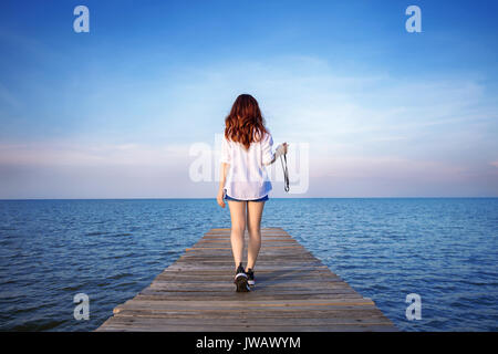 Donna camminando sul ponte di legno estesa nel mare. Foto Stock