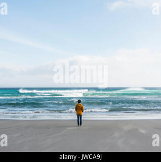 Persona sola in piedi vicino al mare, guardando in lontananza, Sandfly Bay, a Dunedin, Otago, Isola del Sud, Nuova Zelanda Foto Stock