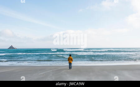 Persona sola in piedi vicino al mare, guardando in lontananza, Sandfly Bay, a Dunedin, Otago, Isola del Sud, Nuova Zelanda Foto Stock