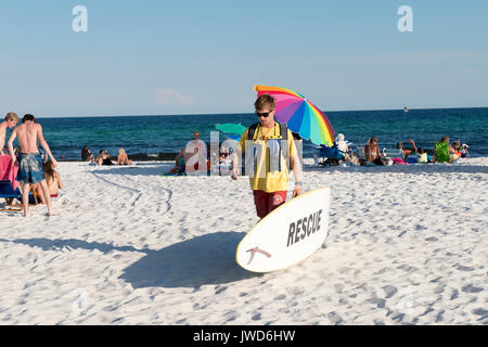 Bagnino passeggiate lungo la spiaggia che porta una scheda di salvataggio Foto Stock