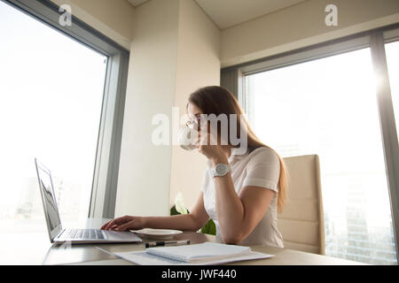 Bella imprenditrice di bere il caffè mentre si lavora sul computer portatile Foto Stock