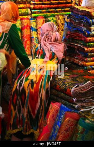 Le giovani ragazze sporgendoti balle di seta colorata a Kashgar bazaar Foto Stock