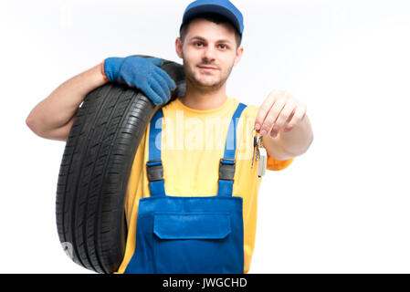 Servizio pneumatici, lavoratore in uniforme blu contiene il pneumatico e la vettura chiavi in mano, sfondo bianco repairman, montaggio ruota Foto Stock