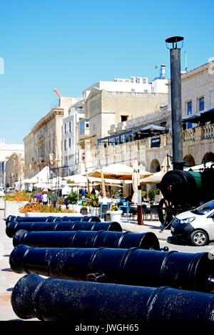 Fila di cannoni lungo il lungomare con caffetterie alla parte posteriore, Vittoriosa (Birgu), Malta, l'Europa. Foto Stock