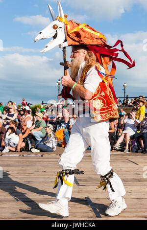 Inghilterra, Broadstairs Settimana della musica folk. Madcap Morris bestia dancing in bright sole estivo. Lunga uomo barbuto tenendo un teschio di animale su un palo sopra la sua testa con orange streamers sospeso verso il basso . Foto Stock