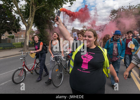 Londra, Regno Unito. Il 12 agosto 2017. Jasmin pietra della messa a fuoco E15 madri detiene un fumo colorato flare su marzo dal punto Ferrier in Canning Town per un rally a Tanner punto in Plaistow sottolineando il pericolo di questi due blocchi con lo stesso rivestimento come Grenfell Tower, esigente di Safe Homes, non sociale pulizia nella zona est di Londra. Poi hanno continuato a i falegnami di estate in Stratford largamente svuotata di persone di oltre dieci anni fa e intende smantellare, per un "mani circa i falegnami di Estate' evento di solidarietà nei confronti di credito: Peter Marshall / Alamy Live News Foto Stock