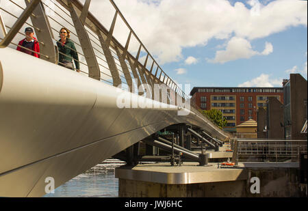 I pedoni attraversano il nuovo ponte pedonale attraverso il nuovo flood barrier sul fiume Lagan a Donegall Quay nel porto di Belfast Irlanda del Nord Foto Stock