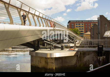 I pedoni attraversano il nuovo ponte pedonale attraverso il nuovo flood barrier sul fiume Lagan a Donegall Quay nel porto di Belfast Irlanda del Nord Foto Stock