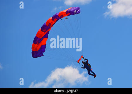 Paracadute colorato contro il cielo blu e bianco delle nuvole feathery. il paracadutismo in caduta libera nel cielo blu Foto Stock