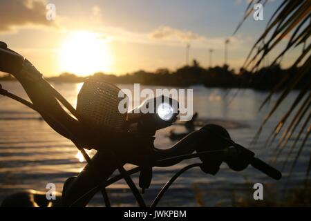 Luce per biciclette illuminata sul manubrio contro il tramonto sul lago Foto Stock