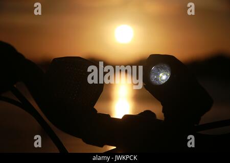 Luce per biciclette illuminata sul manubrio contro il tramonto sul lago Foto Stock