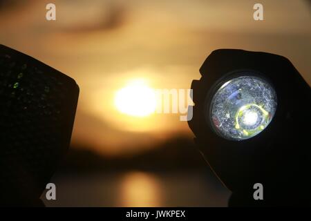 Luce per biciclette illuminata sul manubrio contro il tramonto sul lago Foto Stock