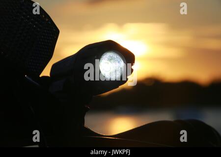 Luce per biciclette illuminata sul manubrio contro il tramonto sul lago Foto Stock