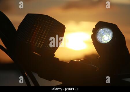 Luce per biciclette illuminata sul manubrio contro il tramonto sul lago Foto Stock