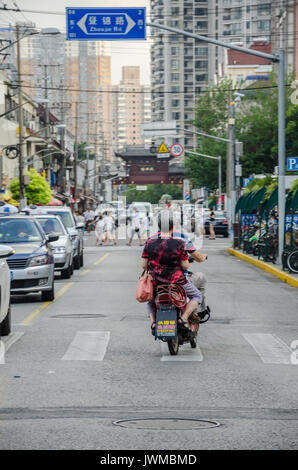 Un giovane cinese un giro in scooter lungo una strada trafficata in Cina a Shanghai. Foto Stock