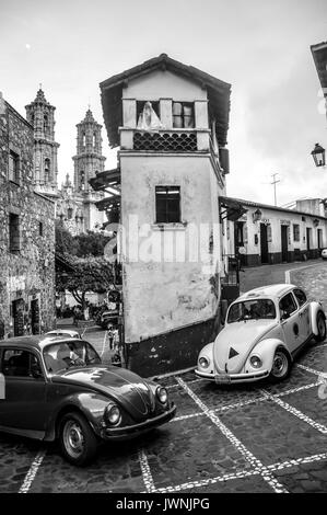 Due Volkswagen maggiolini negoziando una stretta curva inclinata attorno edifici storici in Taxco, Messico meridionale, immagine in bianco e nero Foto Stock