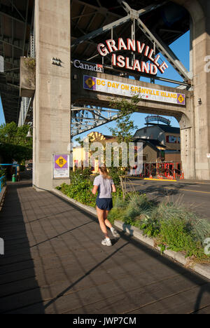 Giovane donna in esecuzione presso l'entrata di Granville Island (sotto Granville Bridge), Vancouver, British Columbia, Canada Foto Stock