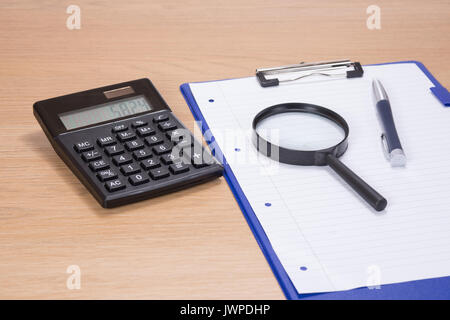 Workstation per ufficio con la calcolatrice, penna e lente di ingrandimento su un foglio bianco di carta su una clipboard giacente su una scrivania di legno in una immagine concettuale Foto Stock