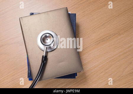 Elevato angolo di visione di uno stetoscopio acustico chestpiece giacente sulla pila di pianificatori contro lo sfondo di legno Foto Stock