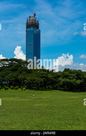 Incompiuta torre di uffici a Shenzhen, Cina, che si affaccia su un parco come un giovane bambino tenta di volare un aquilone Foto Stock