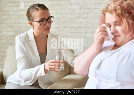 Ritratto di giovane e bella donna che offre un bicchiere di acqua per piangere brevetto femmina durante la terapia sessione sui problemi mentali Foto Stock