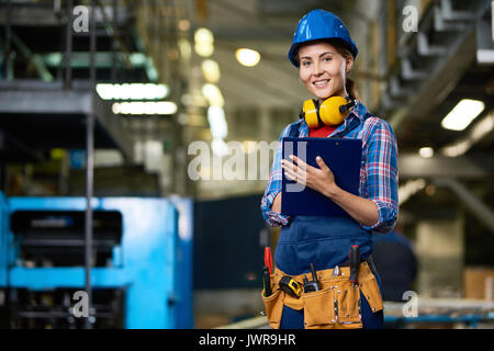 Ritratto di donna lavoratore edile lavora nel moderno impianto guardando la telecamera, sorridente il riempimento in carte negli appunti Foto Stock