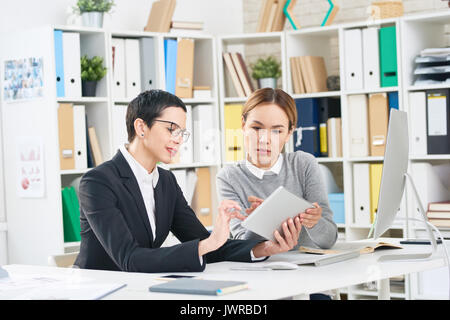I responsabili di concentrato analizzando i risultati del lavoro svolto mentre avente incontro di lavoro in un ufficio moderno, essi con tavoletta digitale Foto Stock