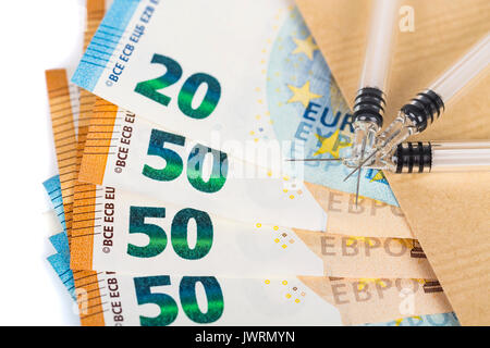 Siringhe e le banconote in euro le fatture in busta marrone. Costo della salute, della medicina, il traffico di droga. Close-up. Foto Stock