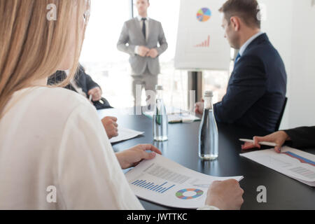Un gruppo di persone di affari ad una riunione di guardare la presentazione di relazioni in diagrammi e grafici alla lavagna a fogli mobili in offfice Foto Stock