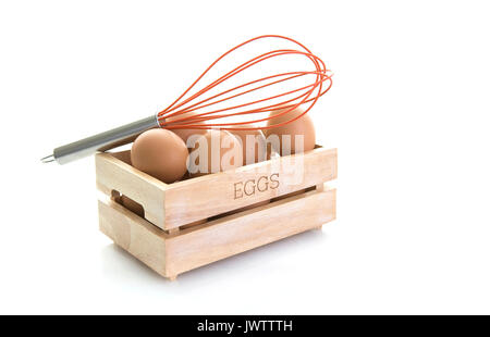 Le uova in una scatola di legno con uovo arancione frusta su sfondo bianco Foto Stock