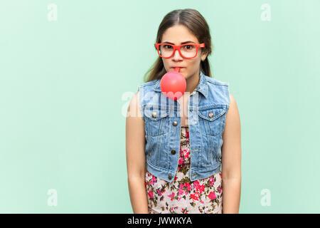 Giovane ragazza felice palloncini di soffiaggio per la festa di compleanno, cercando funny presso la telecamera su uno sfondo verde chiaro. Piscina studio shoot Foto Stock