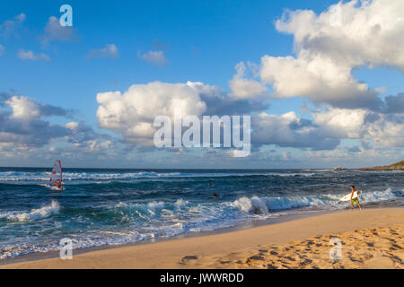 Surfer cammina verso onde come windsurf manzi a shore a Hookipa Beach a Maui Foto Stock