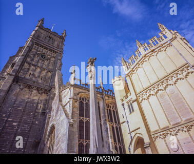 Chiesa di San Giovanni Battista esterno, Cirencester. Soleggiato portico sud sulla destra, con Gesù sulla croce statua nel mezzo. Cotswolds, Inghilterra, Regno Unito. Foto Stock