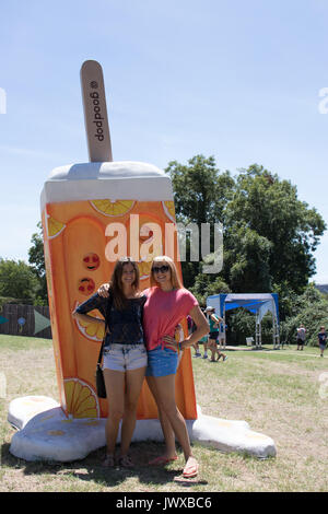 Due giovani donne in piedi accanto a un modello di grandi dimensioni di un arancio ghiaccioli all'aperto presso la Austin Gelato Festival. Alberi e cielo blu in background. Foto Stock