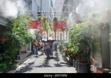 I turisti vagano per le strade di Tianzifang in Cina a Shanghai. Un sistema di raffreddamento spray una nebbia per portare sollievo dal caldo sole. Foto Stock