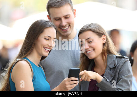 Tre amici a guardare i contenuti multimediali su uno smart phone permanente sulla strada Foto Stock