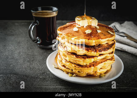 Autunnale di cibi tradizionali. Pila di frittelle di zucca con burro, semi di zucca e sciroppo d'acero. Con una tazza di caffè. Su una pietra nera tabella. Copia sp Foto Stock