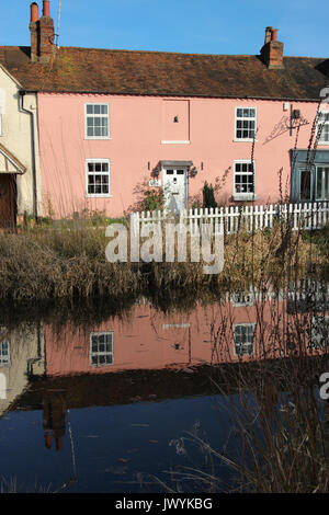 Incantevole vecchio rosa storia due cottage in rurale Bushey, Hertfordshire, Regno Unito, riflesso nel laghetto del paese; il cielo blu, il bianco Picket Fence e ance . Foto Stock