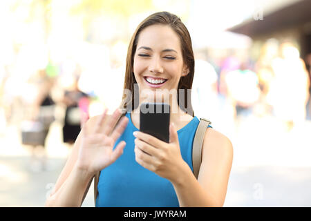 Felice lady saluto durante una chiamata video con uno smart phone su strada Foto Stock