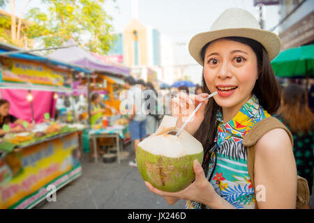 Primo piano della sorridente bella donna ritratto turistico acquistate deliziosi acqua di cocco su travel vacation street mercato all'aperto con tutti i blur bancarelle backgrou Foto Stock